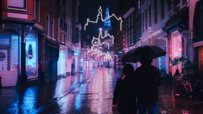 穿黑外套的人在夜间撑着伞在街上行走